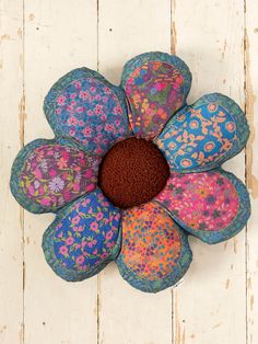 a flower made out of fabric sitting on top of a white wooden floor next to a wall