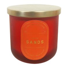 an orange candle with the words sands on it in gold rimmed glass jar against a white background