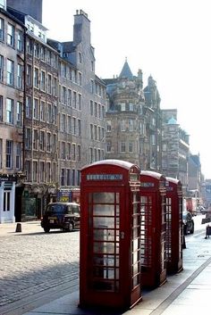 two red telephone booths on the side of a street next to tall buildings and cars