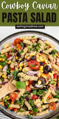 a bowl filled with pasta salad and topped with black olives, tomatoes, corn