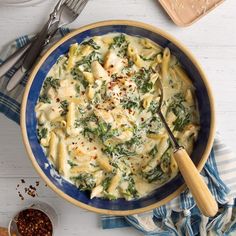 a blue bowl filled with pasta and spinach on top of a white wooden table