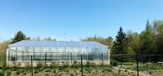 a small greenhouse in the middle of a field with lots of plants and trees around it