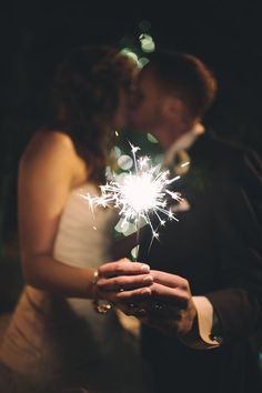 a newly married couple kissing and holding sparklers in their hands as they stand close to each other