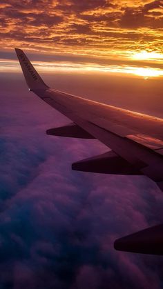 the wing of an airplane as it flies through the sky at sunset or dawn over clouds