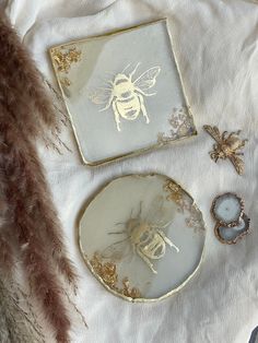 two plates with gold designs on them sitting on a white cloth next to some feathers