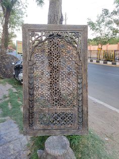 an intricately designed metal sign sitting on the side of a road next to a tree