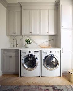 a washer and dryer in a white laundry room with wood flooring, cabinets and rug