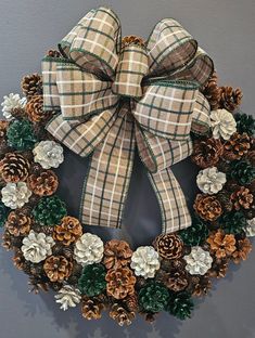 a christmas wreath with pine cones and plaid bow hanging on the wall in front of a gray wall