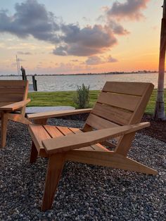 two wooden chairs sitting next to each other on top of a gravel covered ground near the ocean