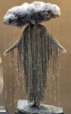 a sculpture made out of cloths and chains hanging from it's head,