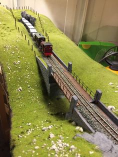 a model train set up on a track with grass and rocks around it, including a bridge