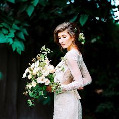 a woman holding a bouquet of flowers in her hand and wearing a white lace dress