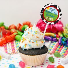 a cupcake with white frosting and sprinkles sits on a table surrounded by candy