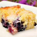 a piece of blueberry cobbler on a plate with purple flowers in the background