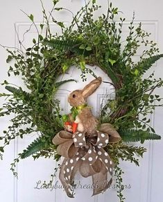 a wreath with a bunny holding carrots and greenery on the front door for easter