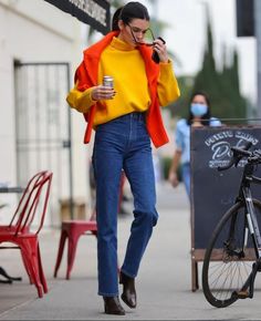 a woman is walking down the sidewalk while talking on her cell phone and drinking coffee