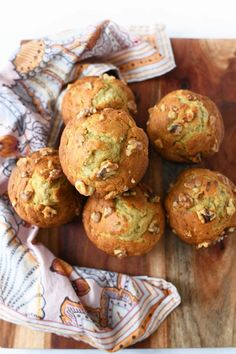 several muffins on a wooden cutting board next to a cloth and napkin with nuts