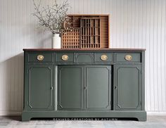 a green cabinet with two doors and some flowers on top, in front of a white wall