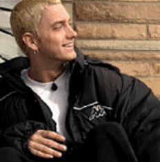 a man with blonde hair sitting on a bench and looking off into the distance while wearing a black jacket