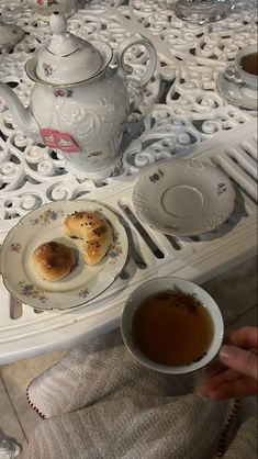 a person holding a cup of tea and plate with pastries on it, sitting at a table