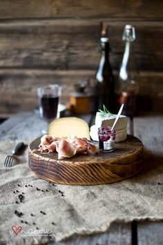 a wooden board topped with different types of cheese and meats next to bottles of wine