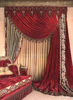 a red bed sitting under a window next to a tall curtained window with curtains on it