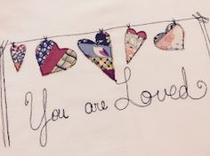 an embroidered t - shirt with hearts hanging on a clothesline that says, you are loved