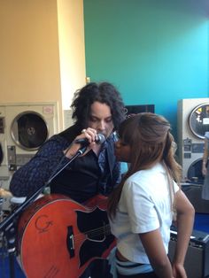 a man holding a guitar while standing next to a woman in front of a microphone