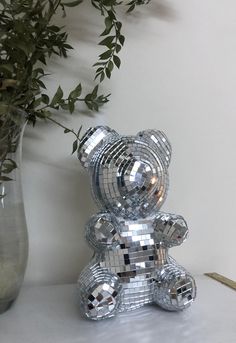 a silver teddy bear sitting on top of a table next to a vase filled with flowers