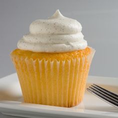 a cupcake with white frosting on a plate next to a fork and knife