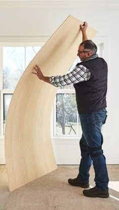 a man standing next to a giant wooden object in a living room with white walls