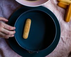 a person is holding a hot dog bun on a blue plate next to other food