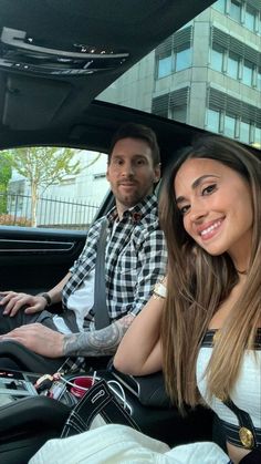 a man and woman sitting in the back seat of a car, smiling at the camera