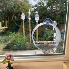 a bird feeder sitting on top of a window sill next to a pink rose