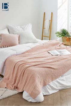 a bed with pink and white blankets on top of it next to a potted plant