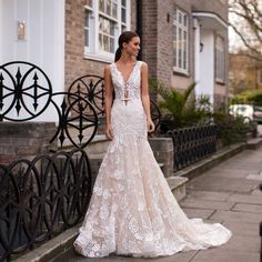 a woman in a wedding dress is standing on the sidewalk near a fence and brick building