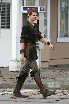 the young man is walking down the street with his hand on his hip and wearing boots