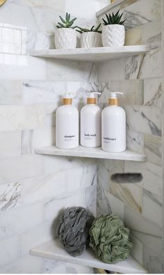 three white bottles are sitting on the shelf in this marble tiled bathroom with green plants