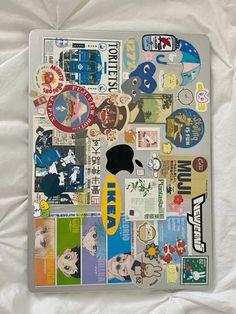 an apple laptop covered in stickers on a white sheet with a pillow behind it