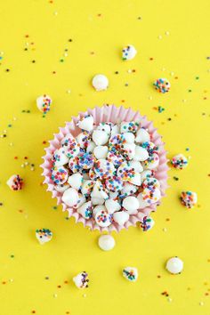 sprinkle covered cupcakes are sitting on a yellow surface surrounded by confetti