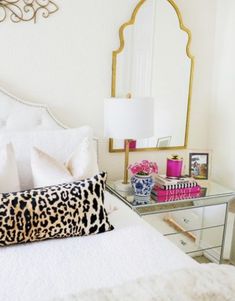 a bedroom with a leopard print pillow on the bed and a gold framed mirror above it