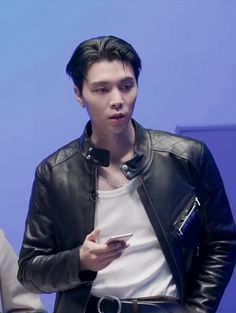 a man wearing a black leather jacket and white shirt holding a cell phone in his right hand