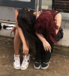 two women are sitting on the ground with their heads down and one is holding her head