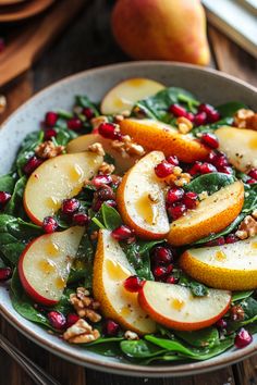 a bowl filled with spinach, apples and walnuts on top of a wooden table