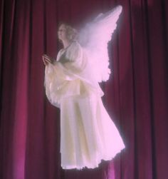 an angel standing in front of a red curtain with her hands folded out and praying