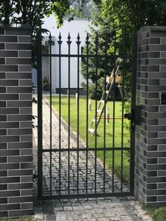 an iron gate in front of a brick wall and green grass with trees on either side