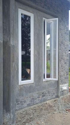 two windows on the side of a house being built with concrete and brick sidings