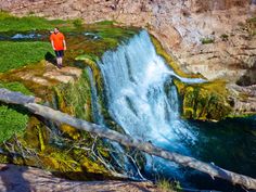 a man standing on the edge of a cliff next to a waterfall with water cascading down it