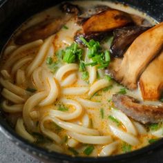 a close up of a bowl of food with noodles and meats in broth