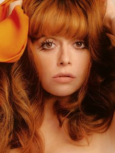 a close up of a woman with long hair and flower in her hair, wearing an orange dress